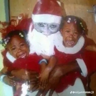 black guy santa with white face paint holding scared kids 